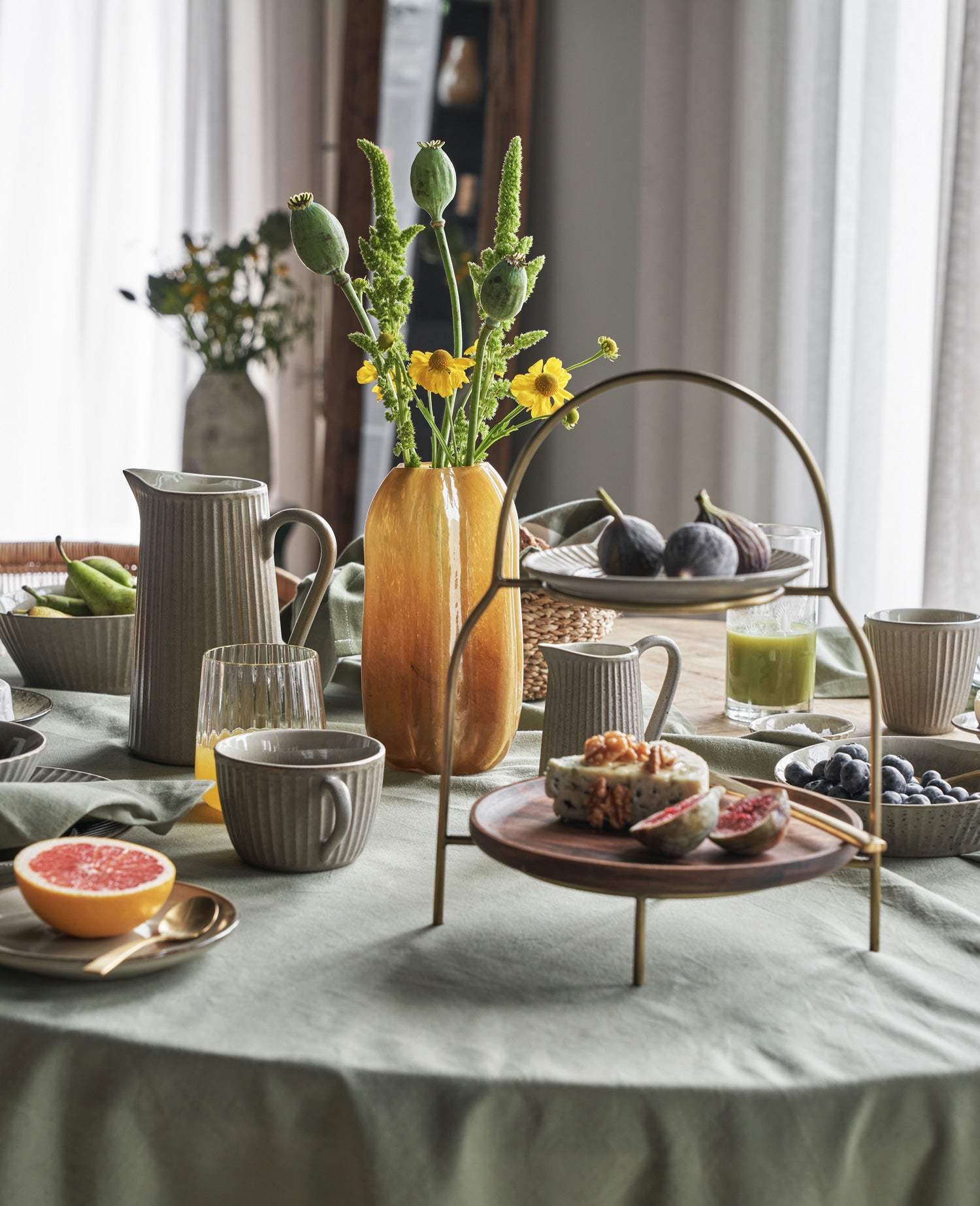 Ein gedeckter Tisch mit graugrüner Tischdecke, geriffeltem Geschirr in taupe, Etagere und Vase mit Blumen.